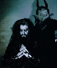 two men dressed up as devil and demon with horns on their heads, standing next to each other