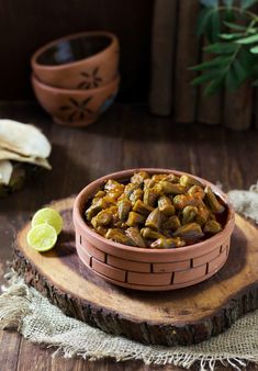 a bowl filled with food sitting on top of a wooden table next to a lime slice