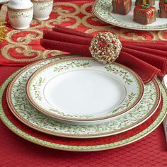 a table set for christmas with plates, silverware and desserts on red place mats