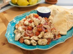 a blue plate topped with chicken and veggies next to a bowl of pita chips