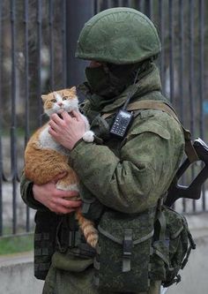 a soldier holding a cat in his arms while standing next to a fence and gate