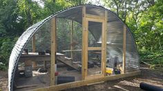 a chicken coop in the middle of some dirt and trees with lots of plants around it