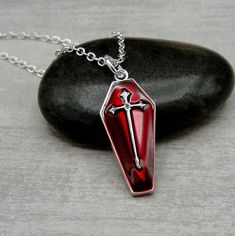 "This Coffin charm necklace comes on a silver-plated chain that is available in different lengths. Please choose your desired length from the drop-down menu when placing the item in your shopping cart.  { CHARM DETAILS } ★ Material: Silver Plated and Enamel  ★ Finish Color: Silver & Red ★ Measurements: 1/2\" x 1\" ★ Dimensions: One-sided { SIMILAR ITEMS }  More Halloween themed items available from my shop: https://www.etsy.com/shop/treasuredcharms/search?search_query=halloween { GIFT OPTIONS } Gift boxes are available at no additional cost and can be added from the drop-down menu during checkout.   You can mark it as a gift, add a gift message, and send it directly to a recipient by entering their address in the 'shipping address' during checkout.  Receipts with price information are not Cross-shaped Halloween Jewelry Gift, Halloween Gift Necklace With Cross Pendant, Halloween Gift Cross Pendant Necklace, Gothic Cross Pendant Jewelry For Halloween, Nickel Free Emo Style Jewelry Gift, Nickel Free Emo Jewelry Gift, Nickel-free Emo Style Jewelry Gift, Emo Necklace With Adjustable Chain For Gift, Gothic Red Nickel-free Necklace