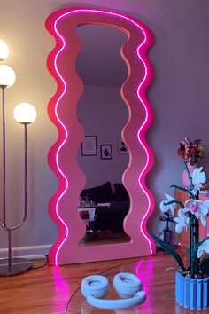 a large pink mirror sitting on top of a wooden floor next to a vase filled with flowers