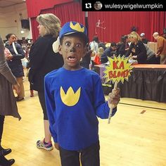 a young boy dressed up as a super hero holding a sign in his right hand