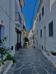 an alley way with white buildings and blue shutters on both sides, surrounded by greenery