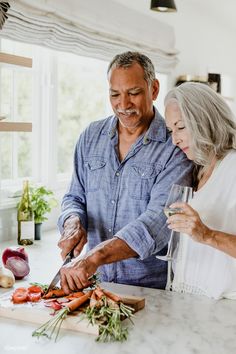 an older man and woman are cutting carrots on the kitchen counter with a knife