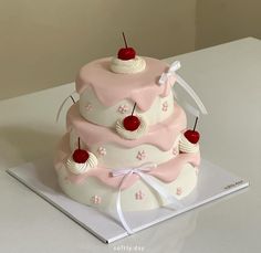 a three tiered cake with cherries and bows on it's top is sitting on a table