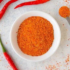 a white bowl filled with spices next to two red chili peppers