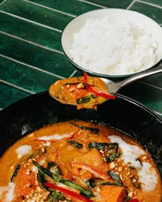 a pan filled with food next to a bowl of rice on top of a table