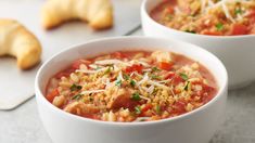 two white bowls filled with soup and topped with parmesan cheese, bread on the side