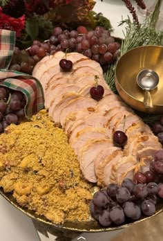 a platter filled with meat and grapes next to other foods on a counter top