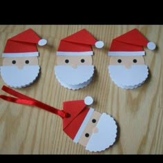 four paper santa claus ornaments on a wooden table