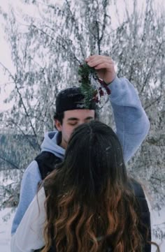 a young man holding up a piece of fruit in front of his face while standing next to a woman