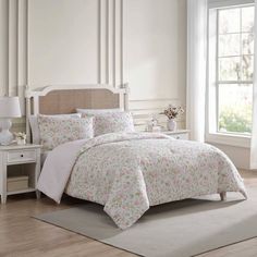 a white bed with pink flowers on it in a room next to a table and window