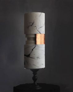 a white and black marble lamp with wood accents on it's base, against a dark background