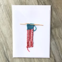 a piece of yarn with a knitting needle on it sitting on top of a white card