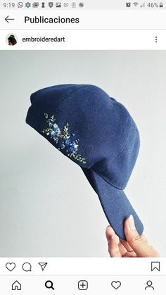 someone is holding up a blue hat with flowers on the brim and side, which has been embroidered onto it