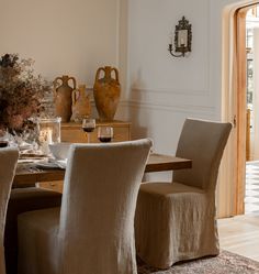 a dining room table and chairs with vases on the wall behind them in front of an open door