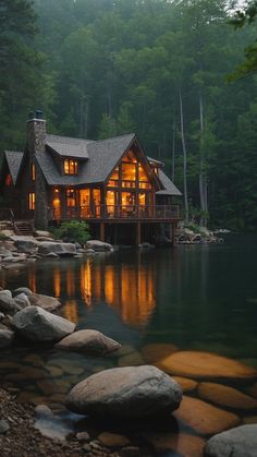 a cabin sits on the shore of a lake at night with its lights on and windows lit up