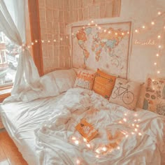 a white bed topped with lots of pillows next to a window covered in string lights