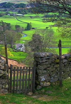 a stone wall and gate with green fields in the background