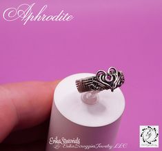 a small silver ring sitting on top of a white tube with the word aphrodite written above it