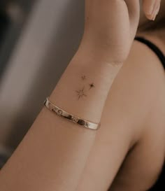 a woman wearing a gold bracelet with a star tattoo on her wrist