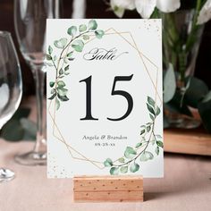 the table numbers are placed on wooden blocks and place cards in front of wine glasses