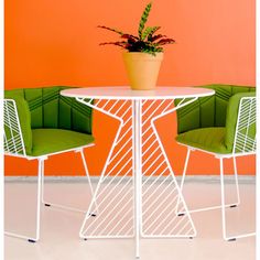 two green chairs and a white table in front of an orange wall with a potted plant on it