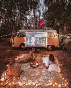 two people sitting on a blanket in front of a vw bus with a screen