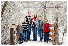 a family poses for a photo on a bridge in the snow with trees behind them