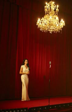 a woman in a white dress is standing on a stage with a chandelier