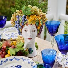 a table topped with plates and glasses filled with grapes, oranges and blue glassware