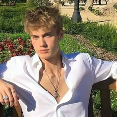 a young man sitting on a bench wearing a white shirt and holding his arm out