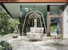 a white swing chair sitting on top of a cement floor next to a table and potted plant