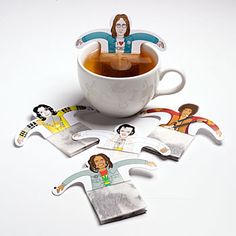 a cup of tea with some stickers on top of it next to a paper cutout of people