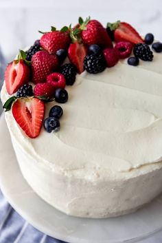 a cake with white frosting and fresh berries on top is sitting on a plate