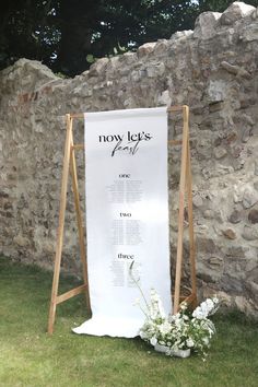 a white sign sitting on top of a grass covered field next to a stone wall