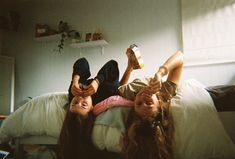 two young women laying on top of a bed next to each other with drinks in their hands