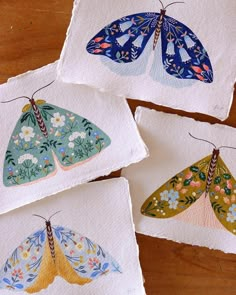 four embroidered butterfly coasters sitting on top of a wooden table