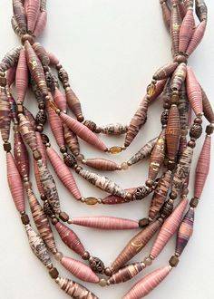 You'll love how effortlessly it is to accessorize with this pink and bronze multi-strand paper bead statement necklace.  Paper bead statement jewelry adds just the right amount of color, style, and flare to your everyday look.  Wear a multi-strand layering necklace, a set of chunky bracelets, or trendy drop earrings for a statement that's not to be ignored.  Materials and Dimensions: -9 strands -Strands Measure 9-15", and the necklace measures 25" from end to end -Colors include pink, brown, bronze, and tan -Other beads included in the necklace: Glass and bronze Each of these homemade pieces of jewelry makes fantastic gifts. Buy one for you and one for her! Let her know how much you care with a colorful statement piece of jewelry for her everyday look!  All pieces come in a burlap drawstri Recycled Beads, Handmade Statement Necklace, Paper Bead Jewelry, Necklace Colorful, Colorful Paper, Gifts For Your Sister, Quilling Cards, Chunky Bracelets, Beaded Statement Necklace