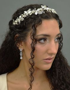 a woman wearing a tiara with flowers on her head and long curly hair is looking at the camera