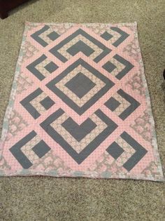 a pink and gray quilt sitting on the floor next to a pair of black shoes