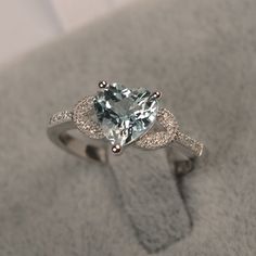 an engagement ring with a heart shaped aquamarinee and diamonds on the side, sitting on top of a gray cloth