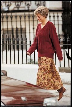 the woman is walking down the street wearing a skirt and sweater with her hand in her pocket