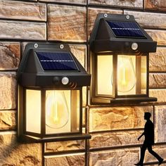 two solar powered lights on the side of a brick wall next to a person walking