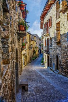 an alley way with stone buildings and potted plants on the windows, in front of a blue sky