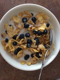 a bowl filled with cereal and blueberries on top of a table next to a spoon