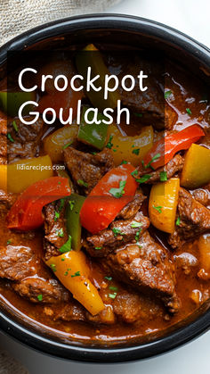 crockpot goulash with peppers and carrots in a black bowl on a white surface